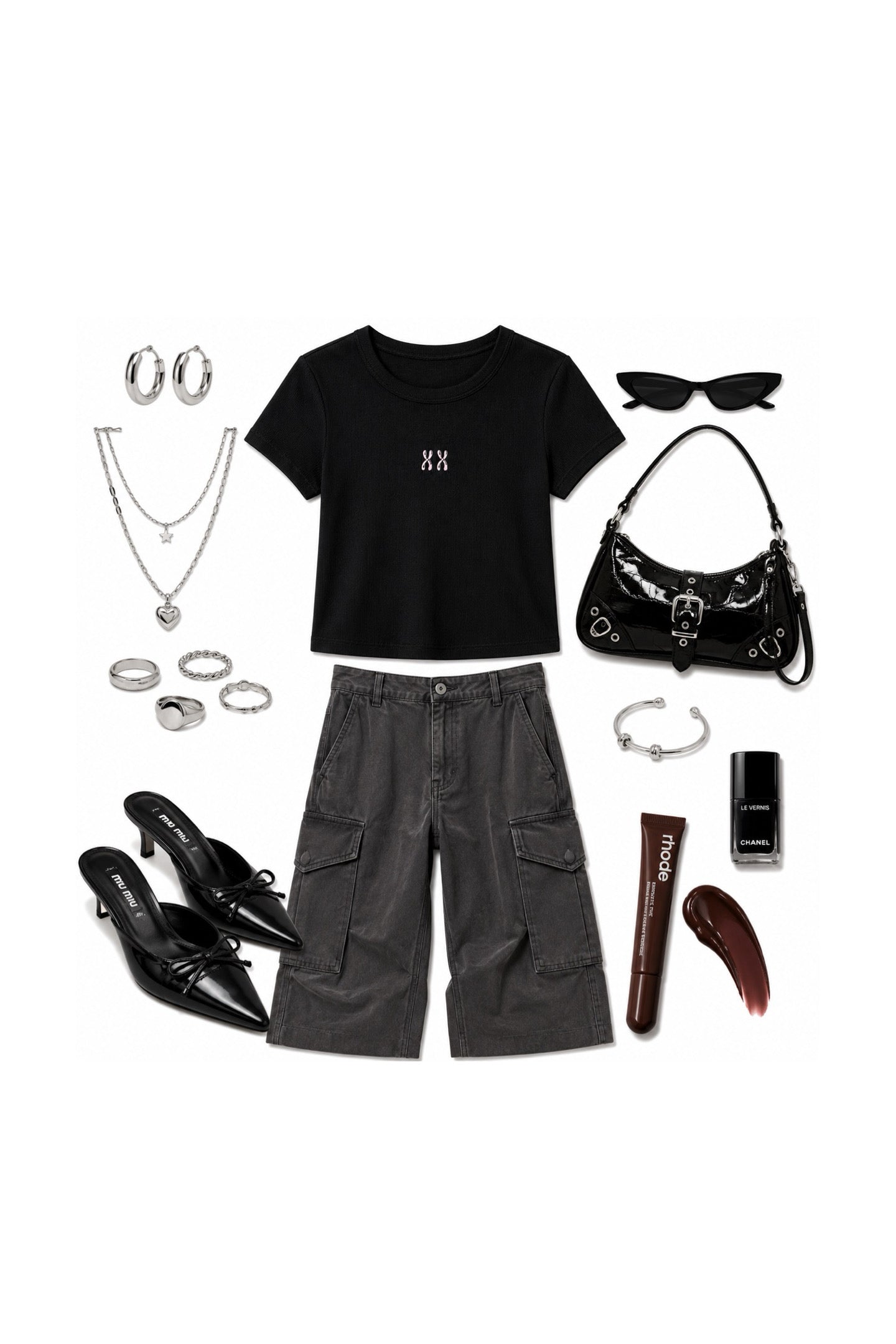 A styled flat-lay outfit on a white background featuring a black short-sleeve crop top with a small white monogram, dark gray cargo shorts, black pointed-toe heels, a black shoulder bag, silver hoop earrings, layered necklaces, rings, sunglasses, a bracelet, and a lip gloss tube.